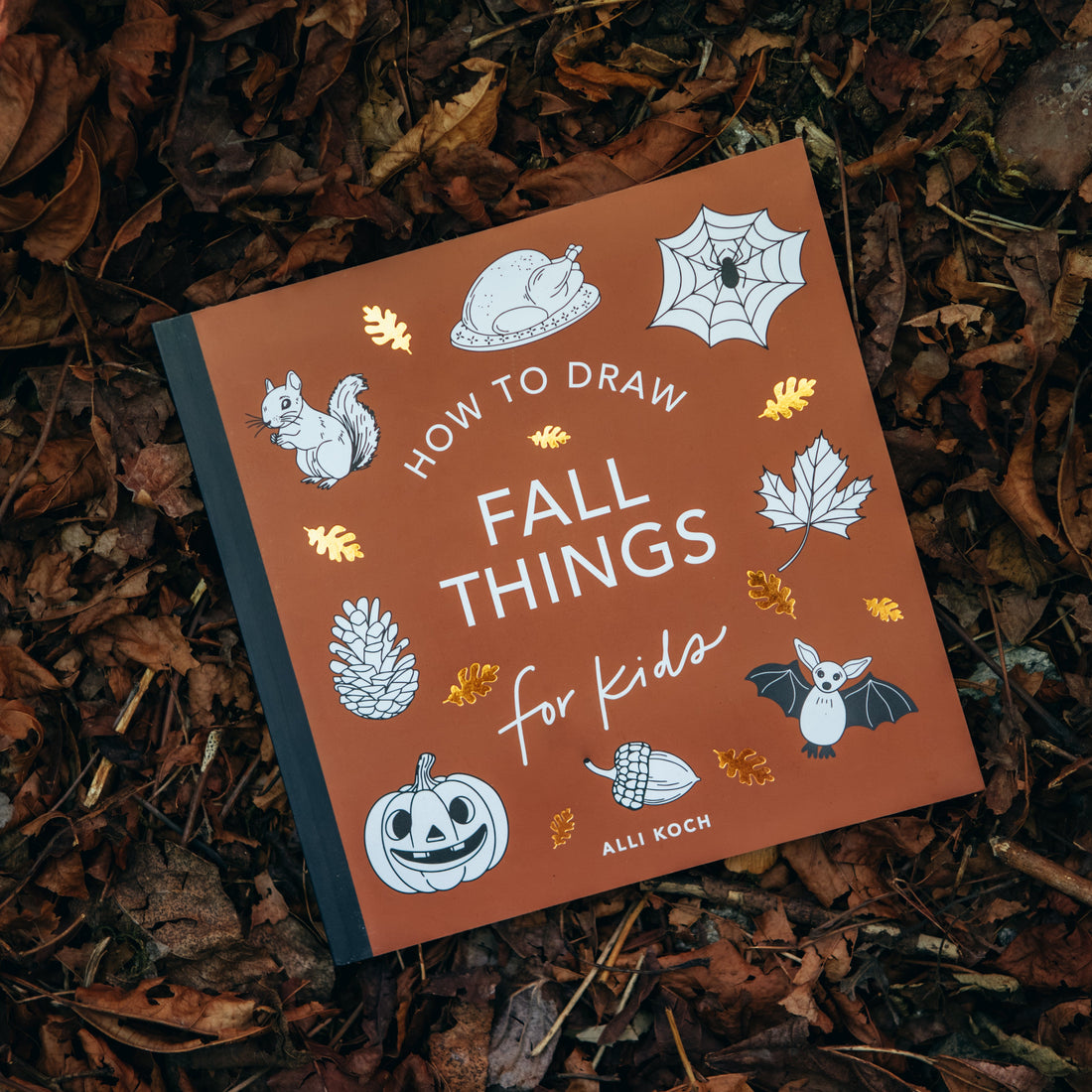 Book titled 'How to Draw Fall Things for Kids' on a bed of leaves