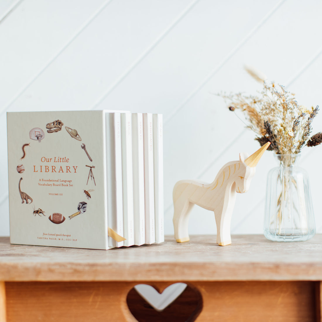 Book titled 'Our Little Library' on a wooden surface with a unicorn figurine and vase of dried flowers.