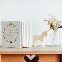 Book titled 'Our Little Library' on a wooden surface with a unicorn figurine and vase of dried flowers.