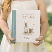 Young girl holding a book titled 'Our Little Adventure of Easter' with an illustration of a rabbit and basket on the cover.