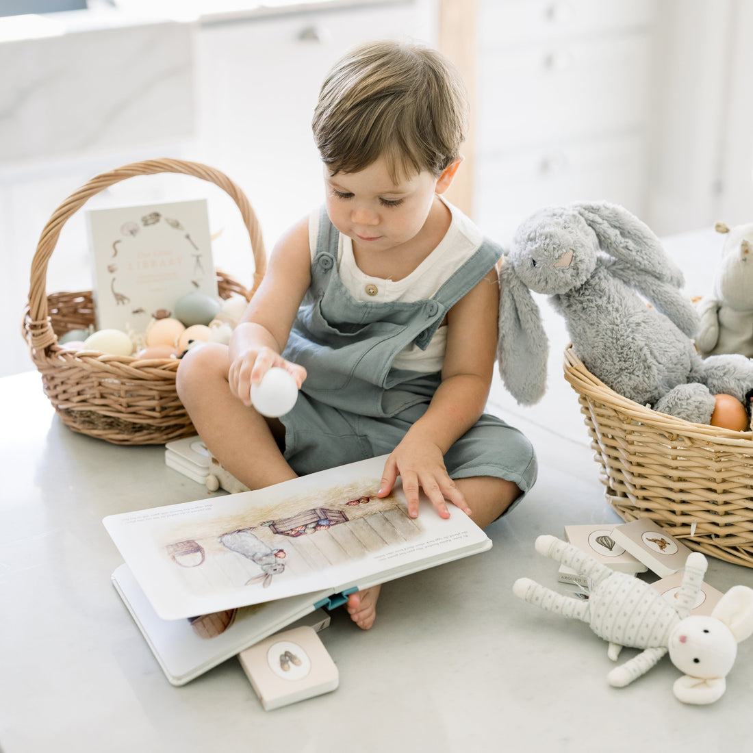 Child reading a book with toys on a light-colored floor