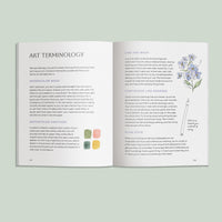 Open book showing art terminology with illustrations on a light green background