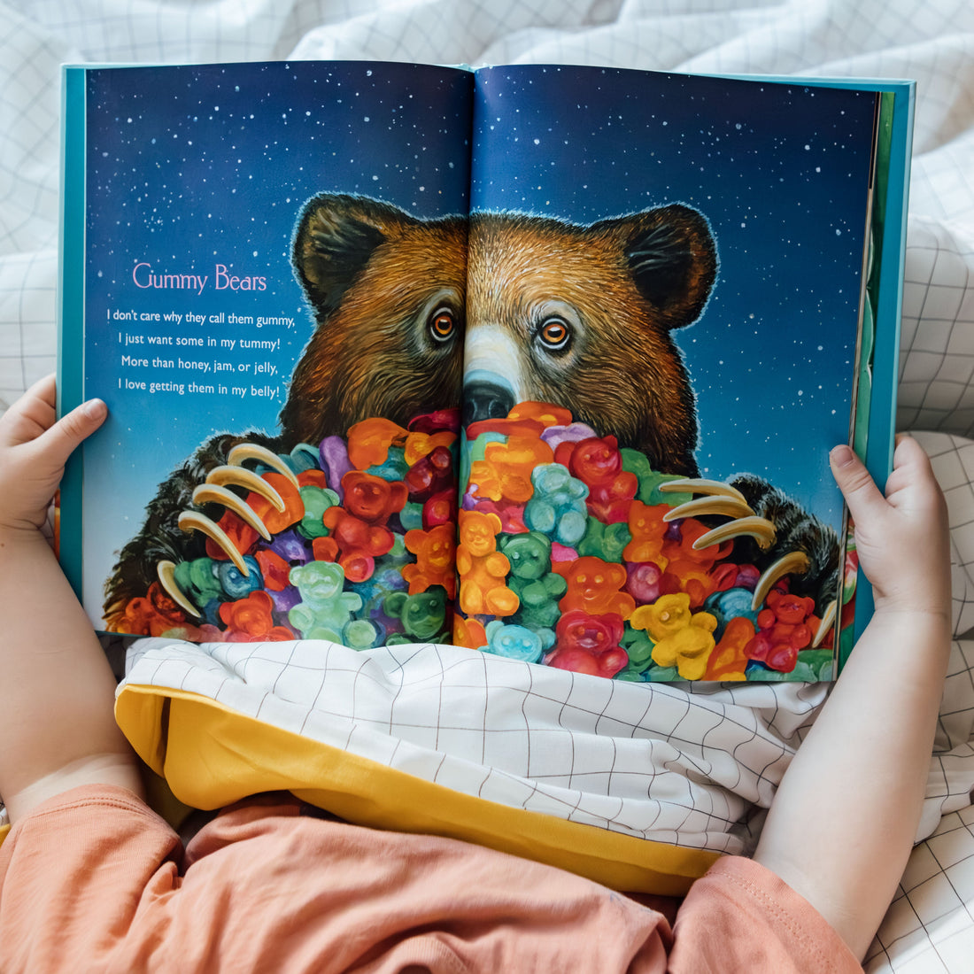 Child reading a book with a colorful bear illustration on a bed