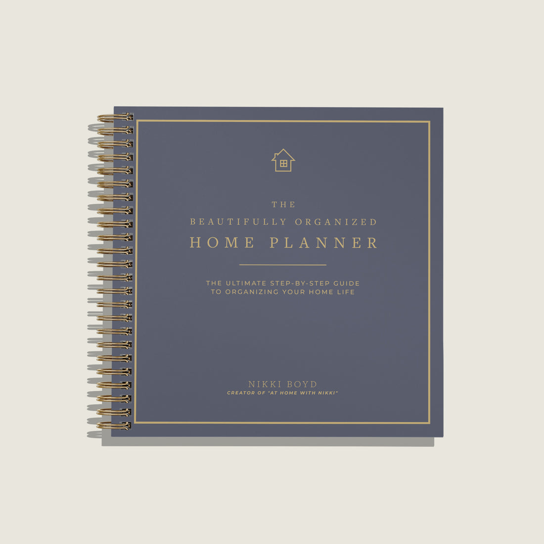 A spiral-bound home planner book titled 'The Beautifully Organized Home Planner' by Nikki Boyd, featuring a slate blue cover with gold text and border details, shown on a light beige background.