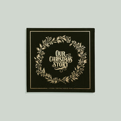 A green and gold Our Christmas Story memory book with a floral wreath design on the cover.
